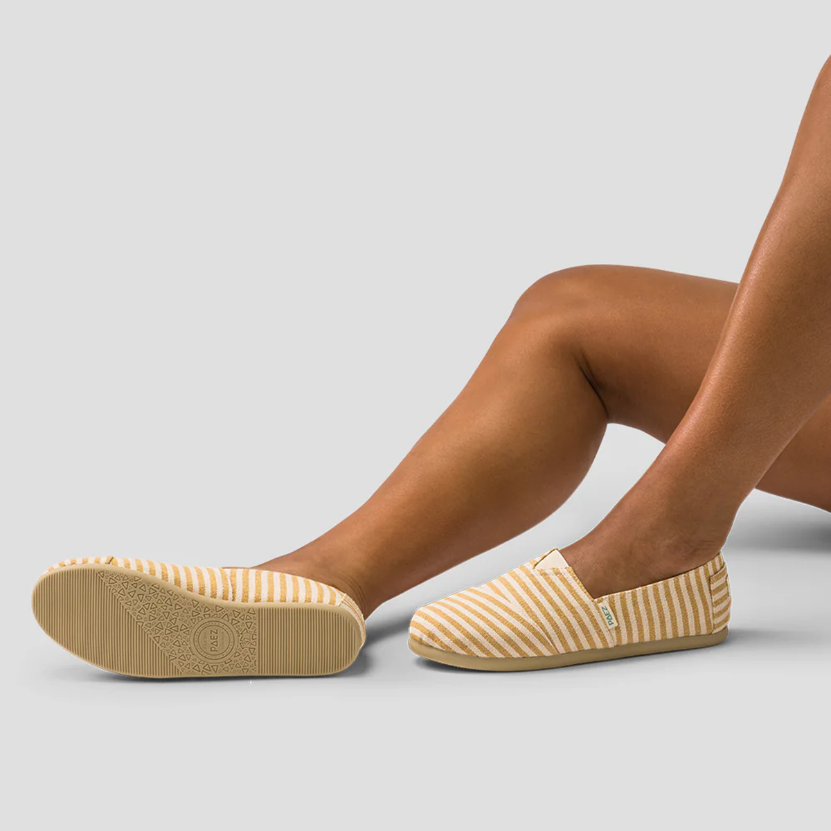 Caramel PAEZ Surfy espadrille shoes for women, featuring caramel and cream striped fabric, shown with non-slip rubber soles while worn in a relaxed pose against a plain grey background.