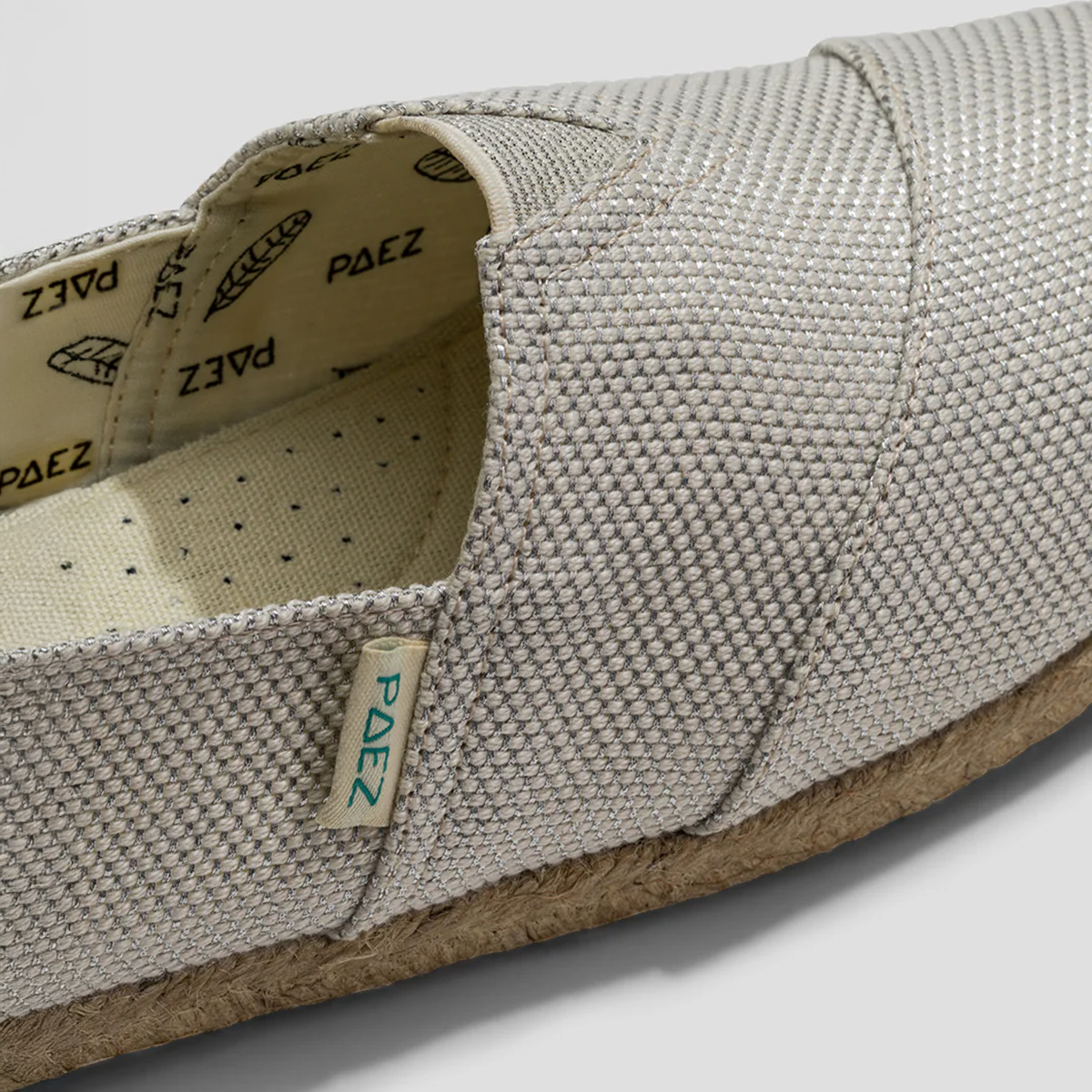 Close-up of Classic Silver PAEZ espadrille shoe for women showing the textured fabric and jute sole, with the PAEZ brand tag visible.
